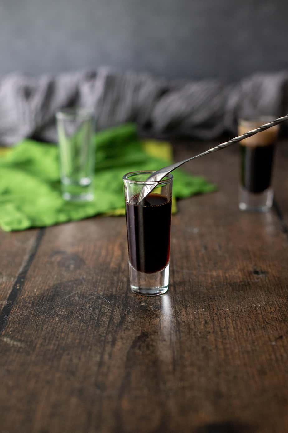 a shot glass with coffee liqueur and bar spoon, showing how to pour a layered shot.