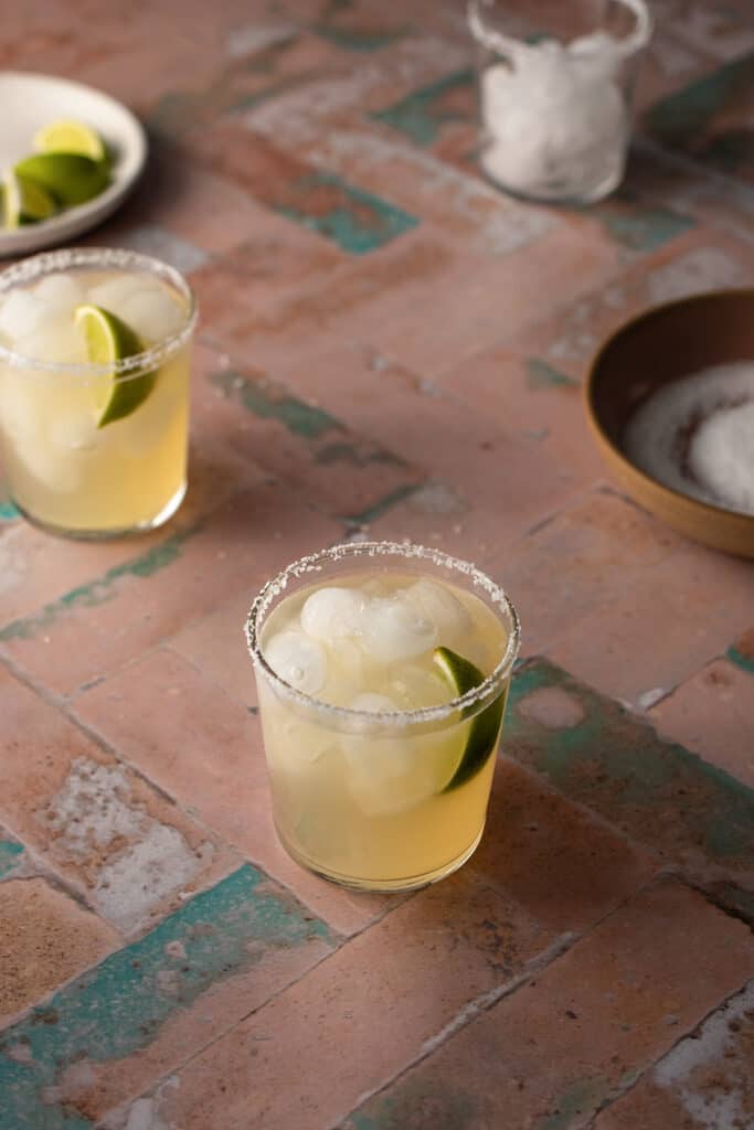 2 golden margaritas on a pink and green tile background