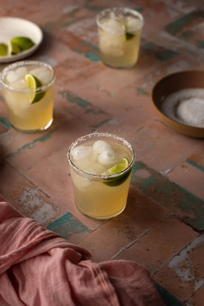 3 golden margaritas on a pink and green tile background