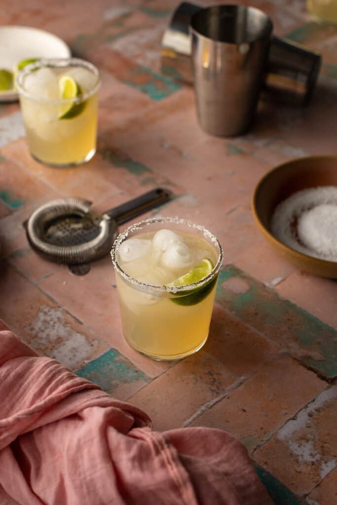 2 golden margaritas on a pink and green tile background