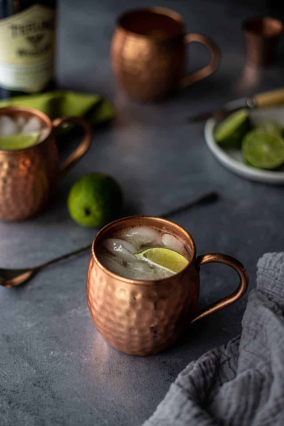 two Irish Mule cocktails in copper mugs on a gray background
