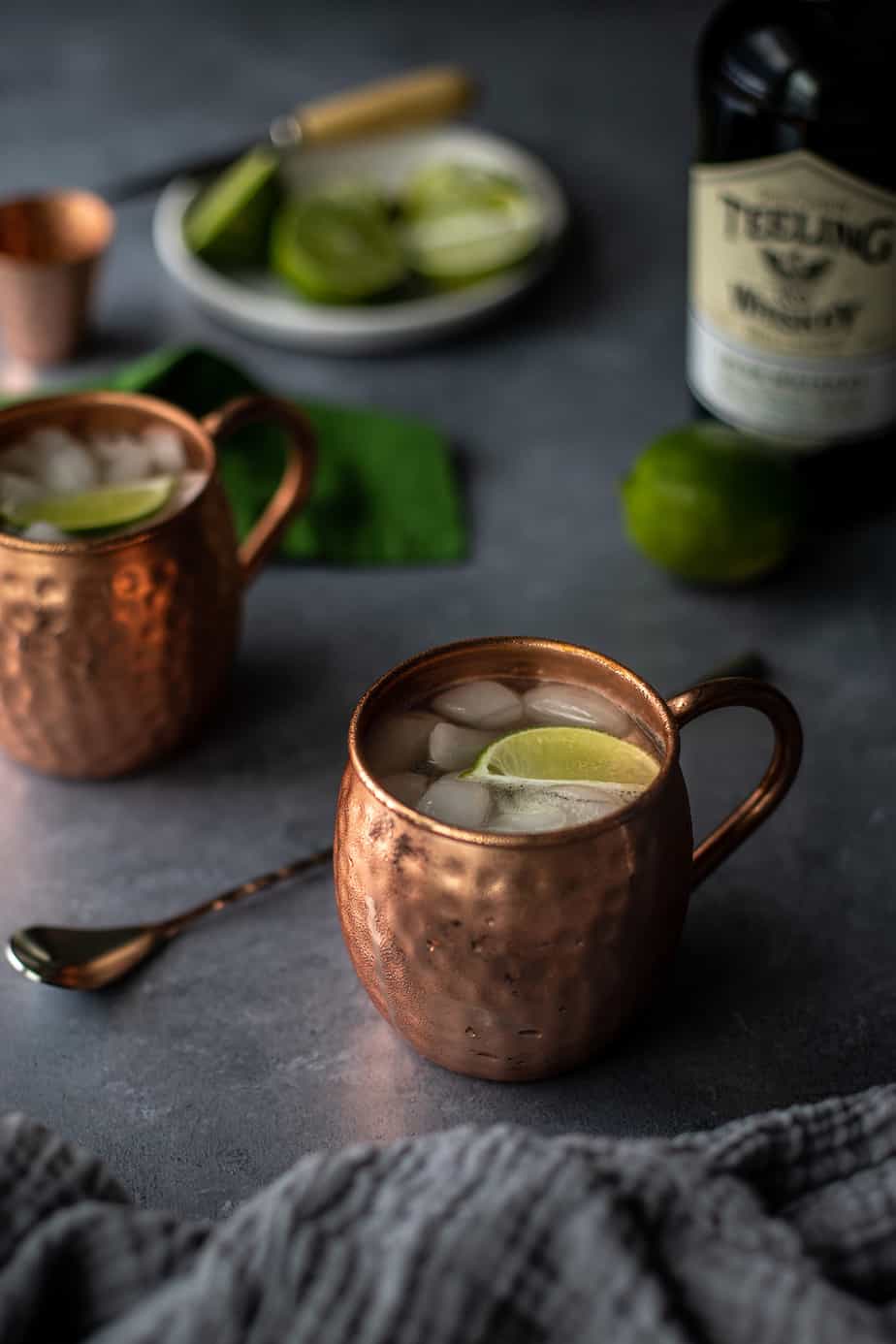 two Irish Mule cocktails in copper mugs on a gray background