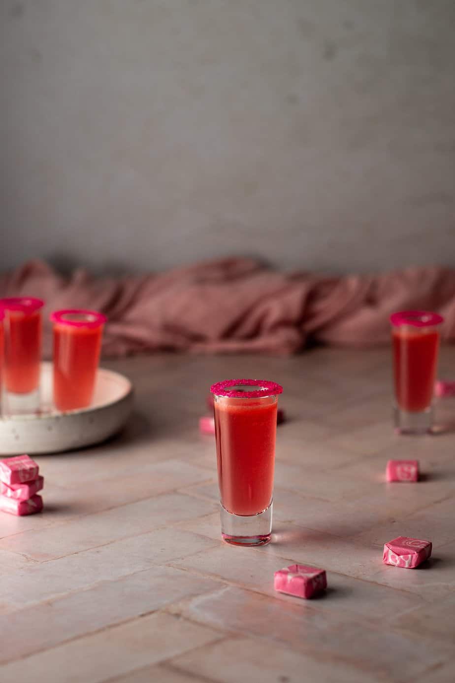 4 shot glasses filled with pink starburst shots