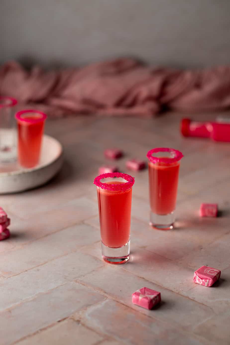 4 shot glasses, 3 filled with pink starburst shots