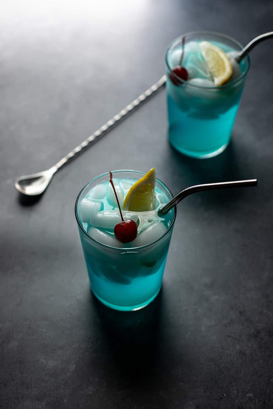 backlit photo of two glasses filled with a light blue liquid and ice