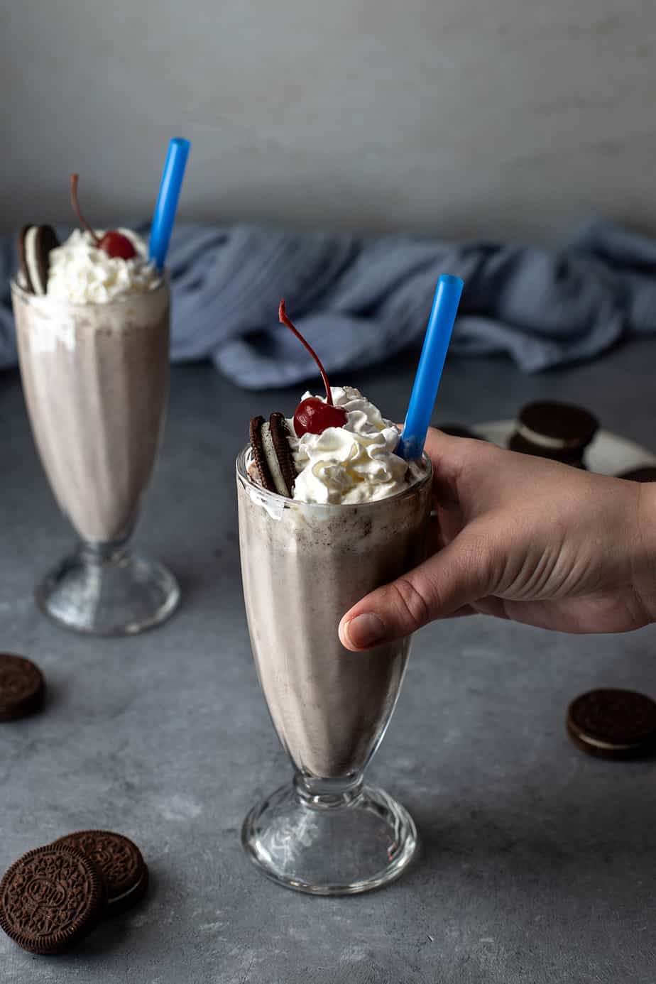 a hand grabbing a glass with a cookies and cream milkshake