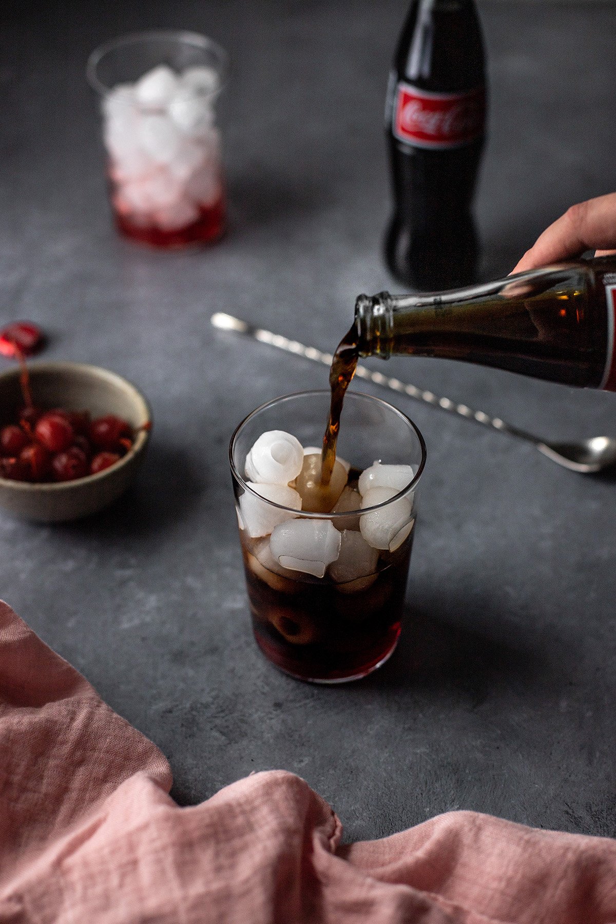 Coke being poured into a tall glass with ice and grenadine.