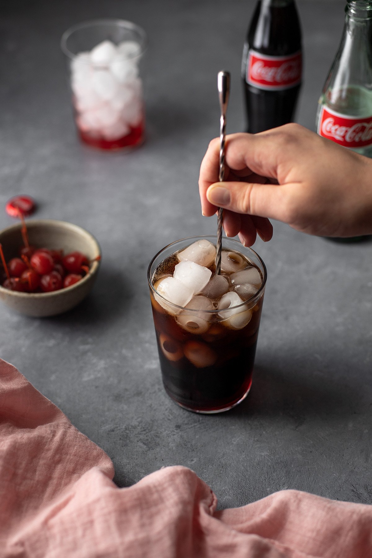 45 degree angle view of a hand, holding a bar spoon, stirring a roy rogers drink.