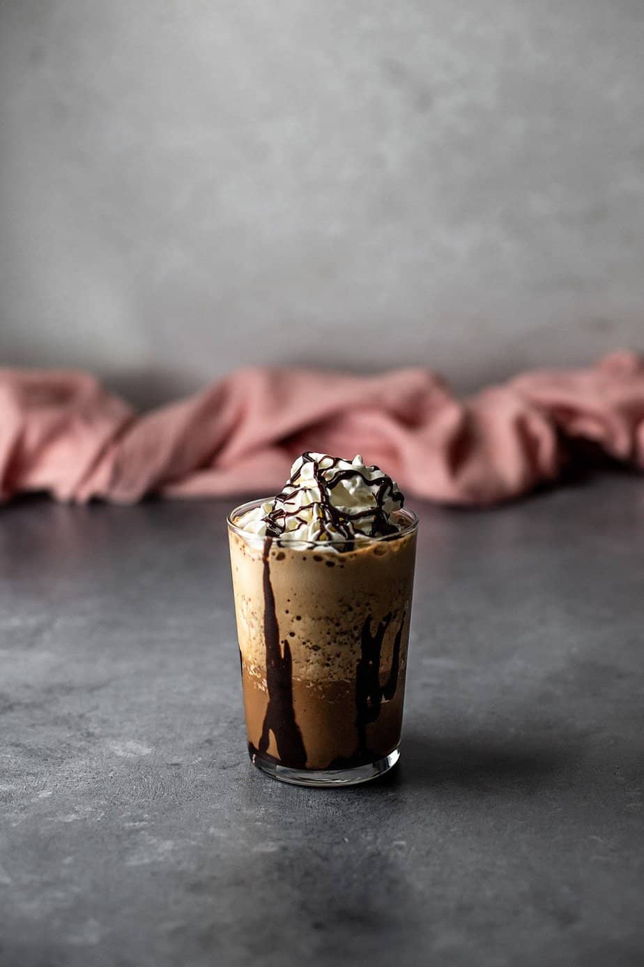 a java chip frappuccino in a glass, topped with whipped cream and chocolate sauce