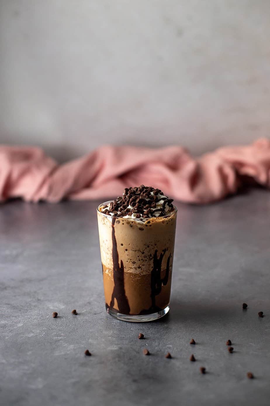 a java chip frappuccino in a glass, topped with whipped cream, chocolate sauce, and probably too many mini chocolate chips