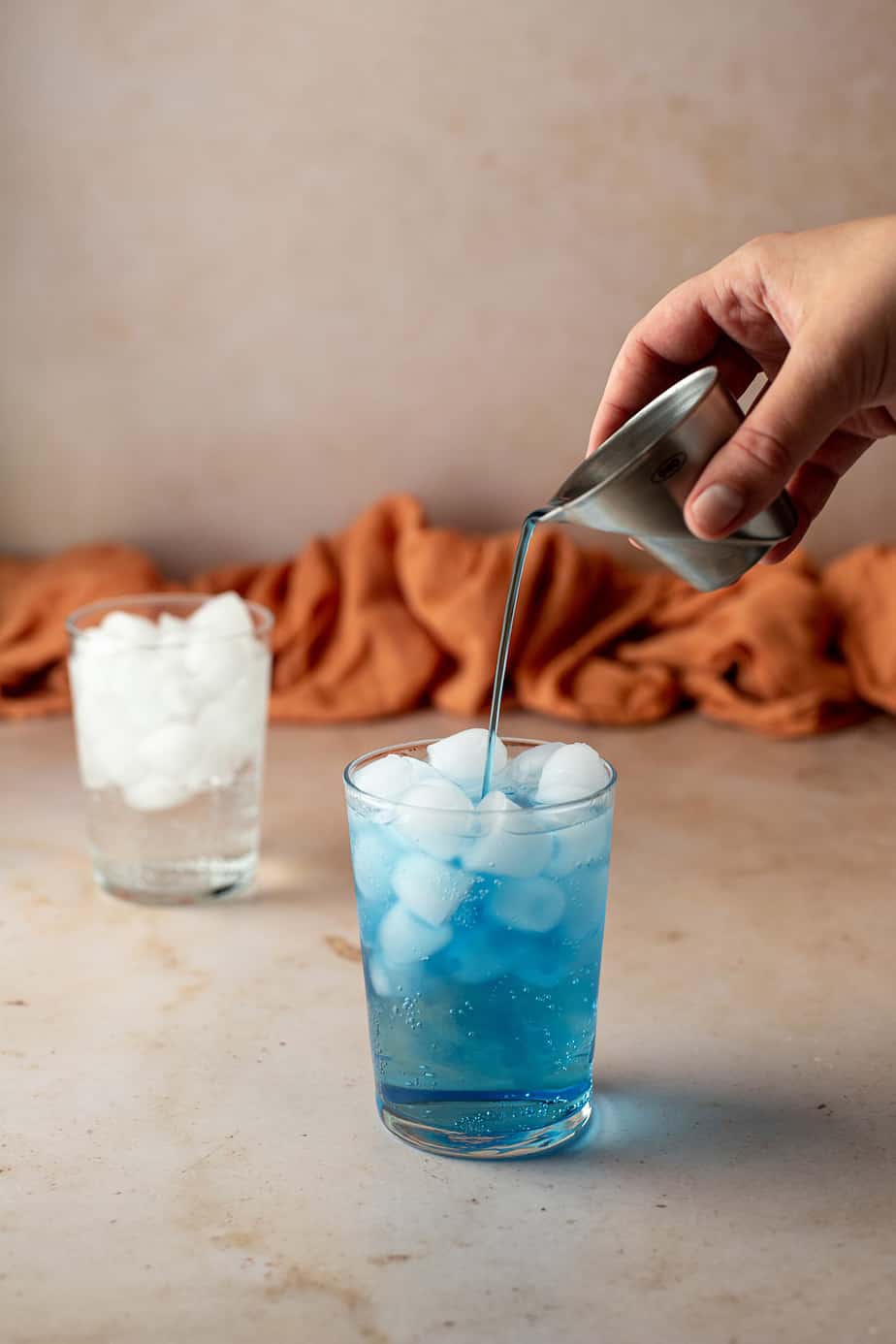 blue syrup being poured into a glass of Sprite with ice