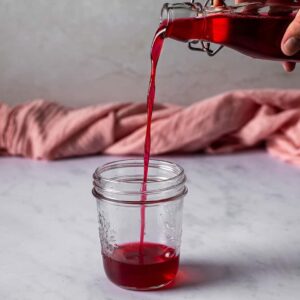 cherry simple syrup being poured from a glass bottle into a glass jar