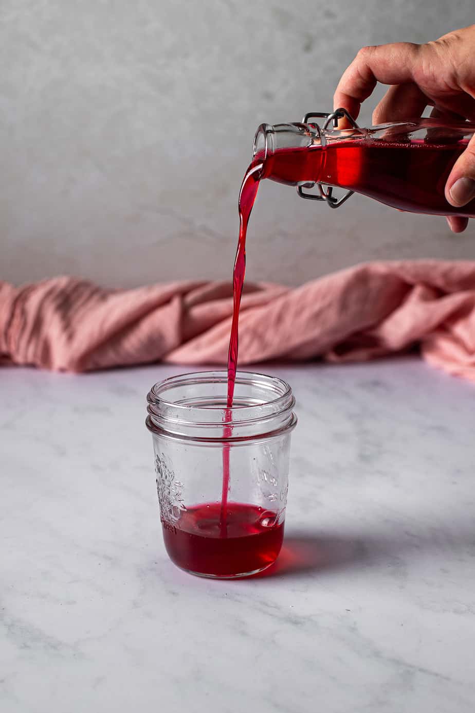 cherry simple syrup being poured from a glass bottle into a glass jar