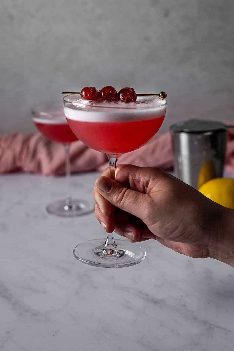 a hand holding a coupe glass full of a cherry vodka sour.