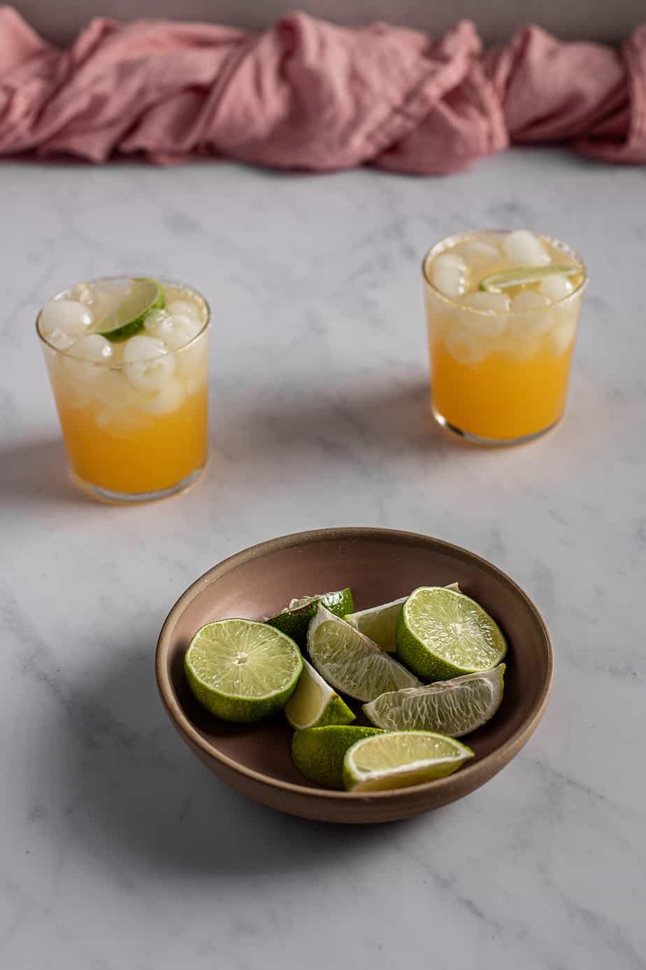 a pink bowl full of lime slices in the foreground, two virgin margaritas in the background