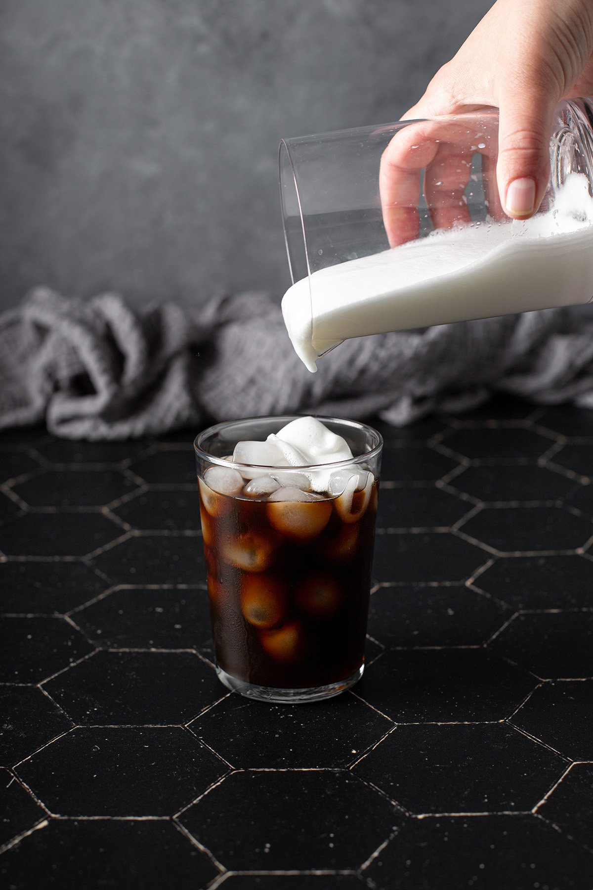 pouring cold foam onto a glass of cold brew coffee