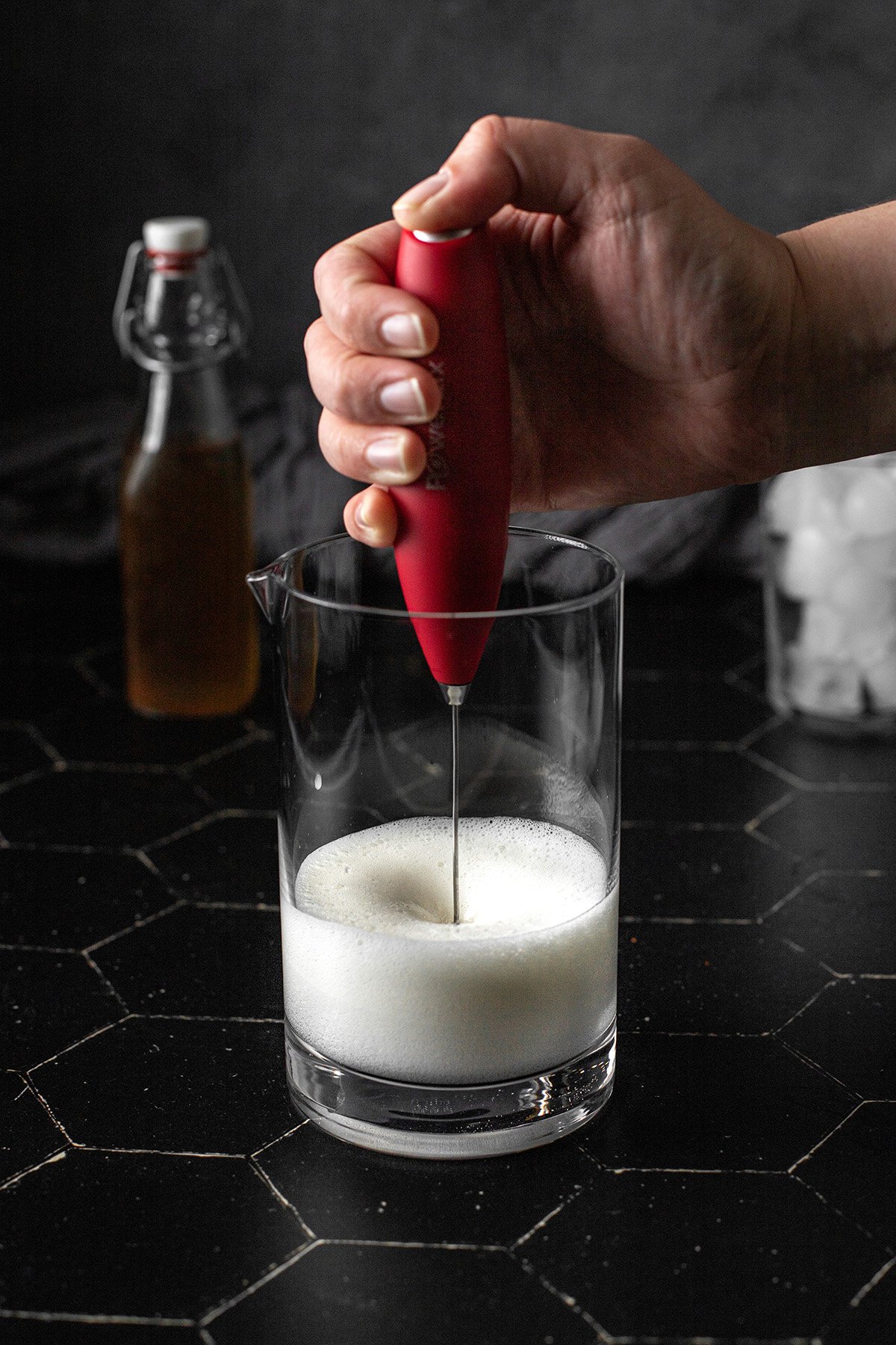 a hand milk frother whipping up milk in a glass container