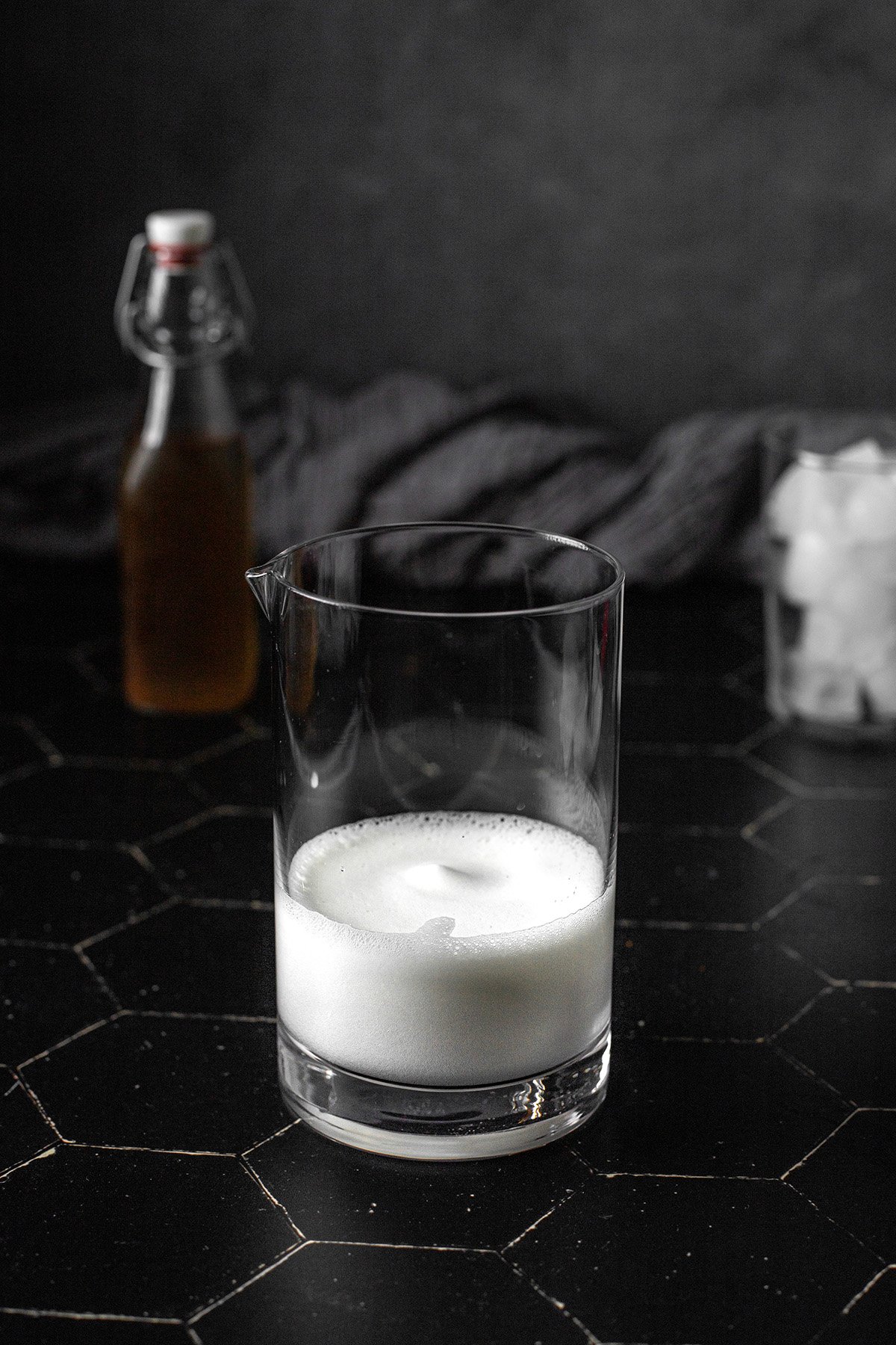 a glass container with frothed up milk and sweetener