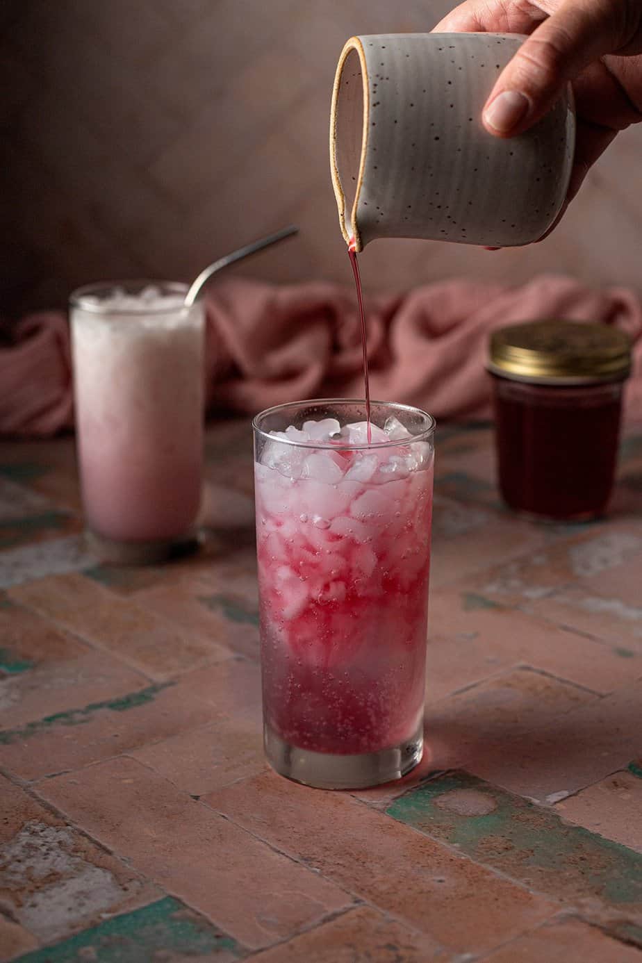 a tall glass with crushed ice and club soda, with cherry simple syrup being poured in