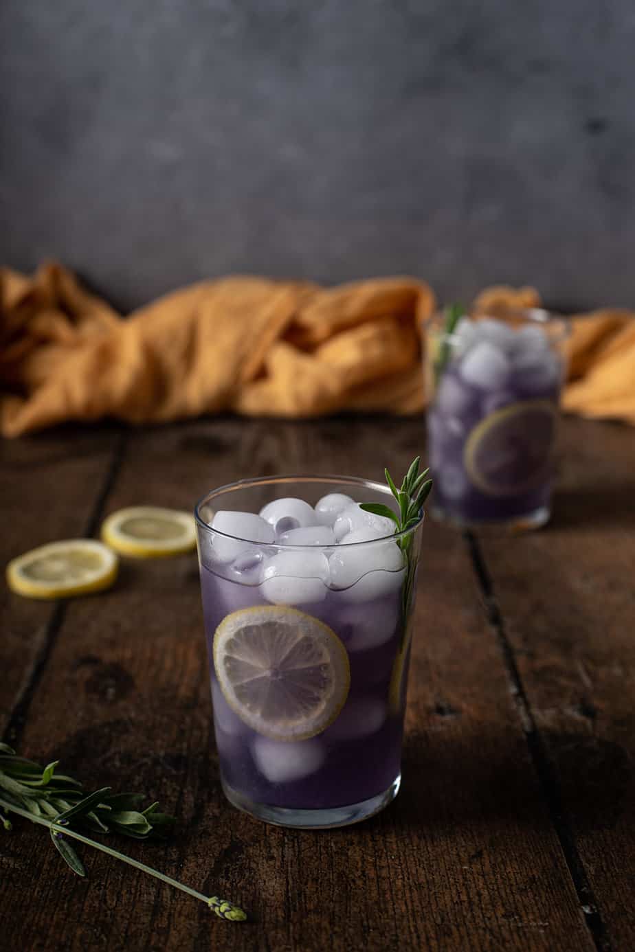 two glasses of lavender lemonade garnished with lemon wheels and lavender sprigs