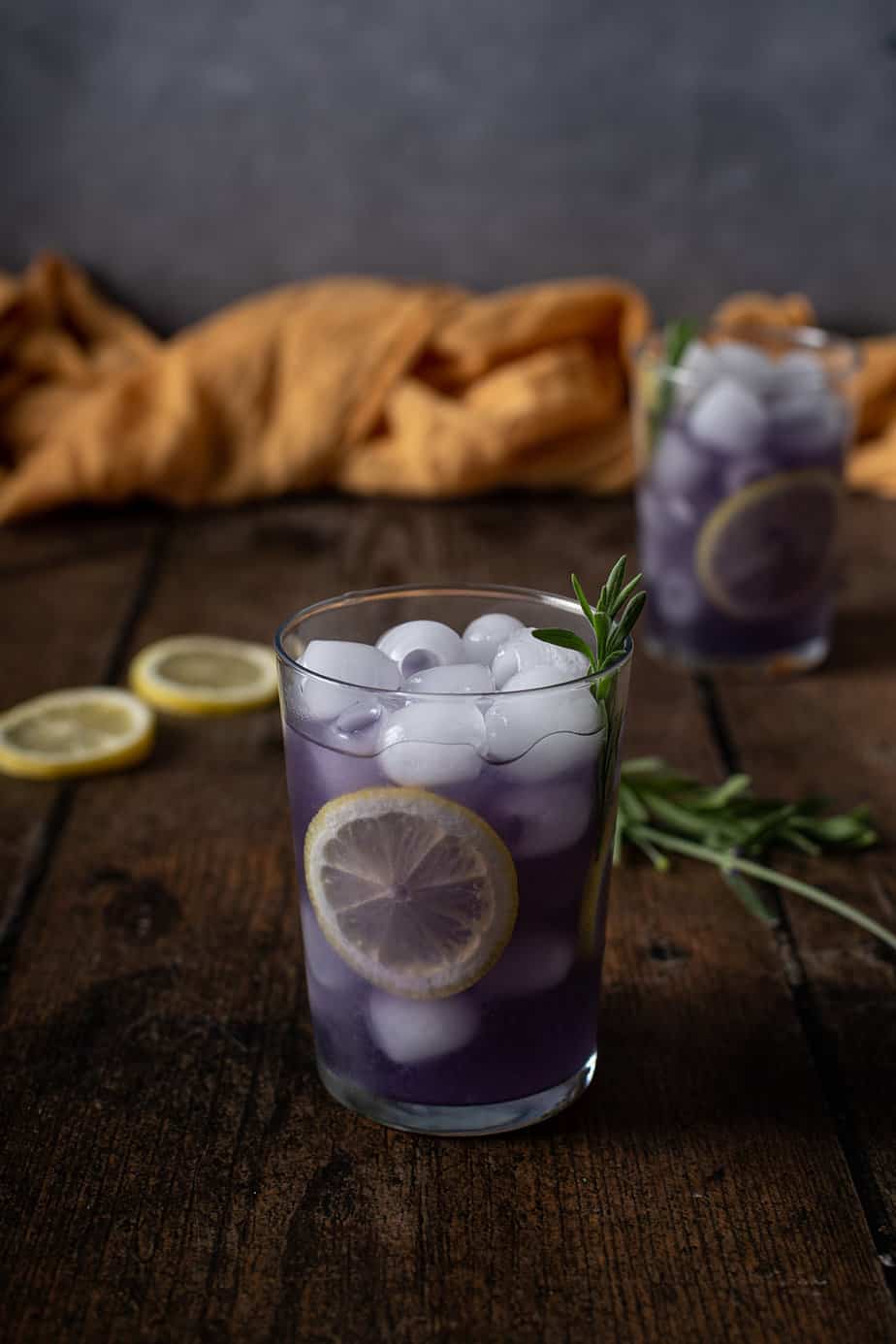 two glasses of lavender lemonade garnished with lemon wheels and lavender sprigs