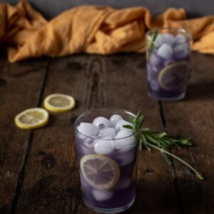 two glasses of lavender lemonade garnished with lemon wheels and lavender sprigs