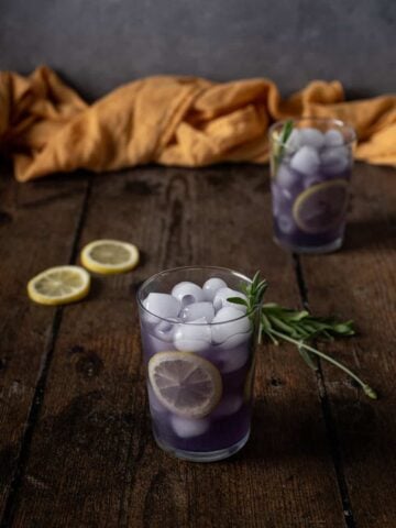 two glasses of lavender lemonade garnished with lemon wheels and lavender sprigs
