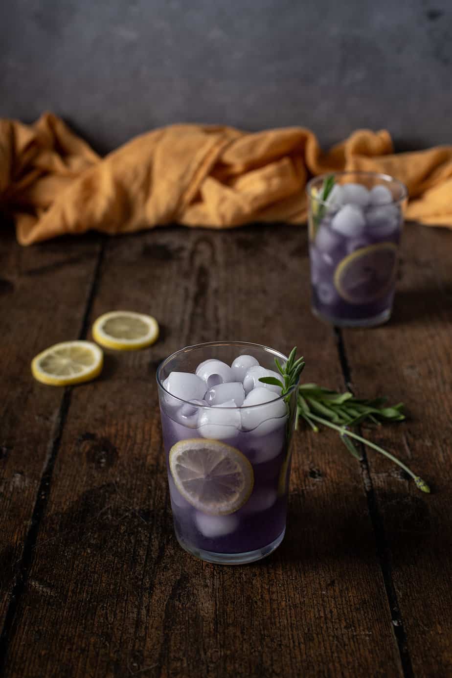 two glasses of lavender lemonade garnished with lemon wheels and lavender sprigs