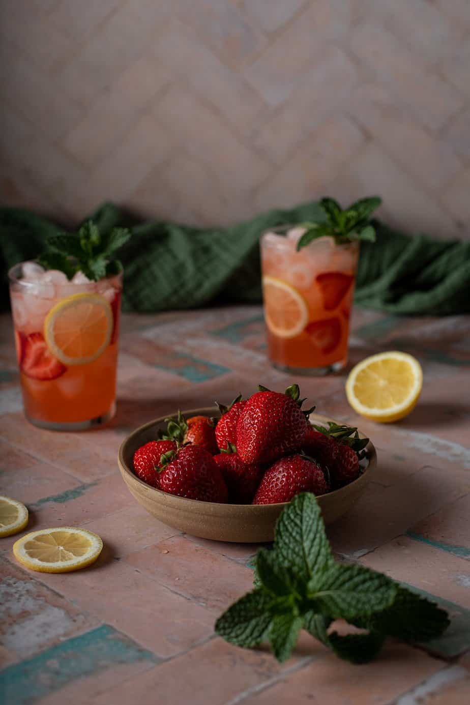 a bowl of strawberries, two glasses with strawberry lemonade and vodka in the background