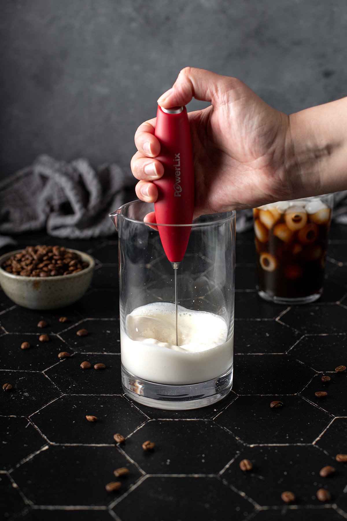 a hand holds a milk frother, frothing liquid in a glass container.