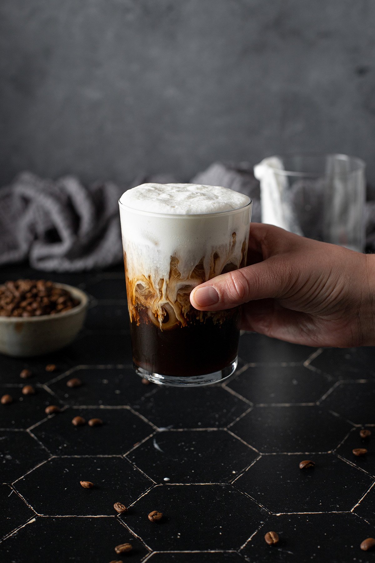 a hand holding a glass of cold brew coffee topped with vanilla sweet cream cold brew