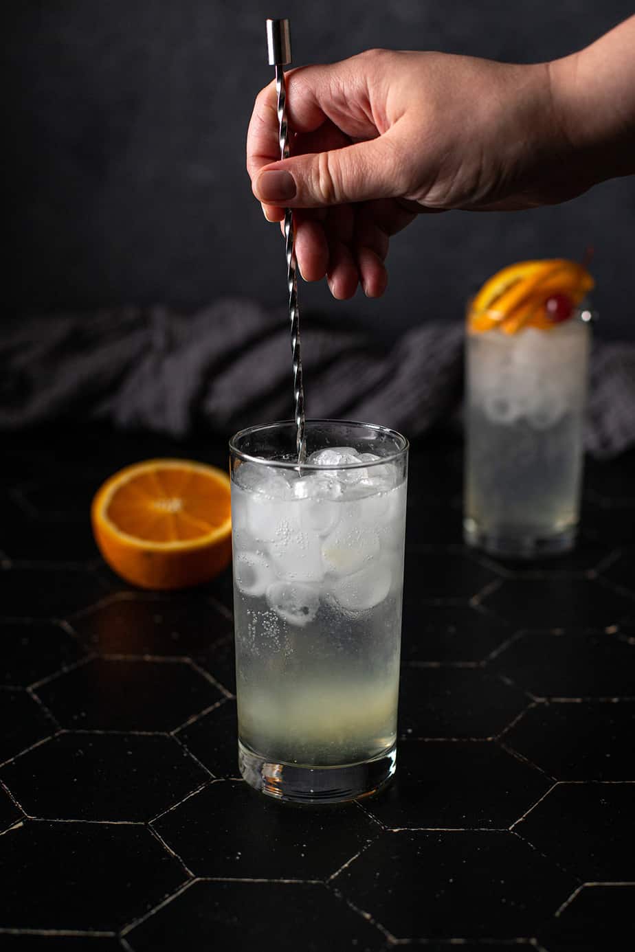 hand stirring a glass of vodka collins with a bar spoon
