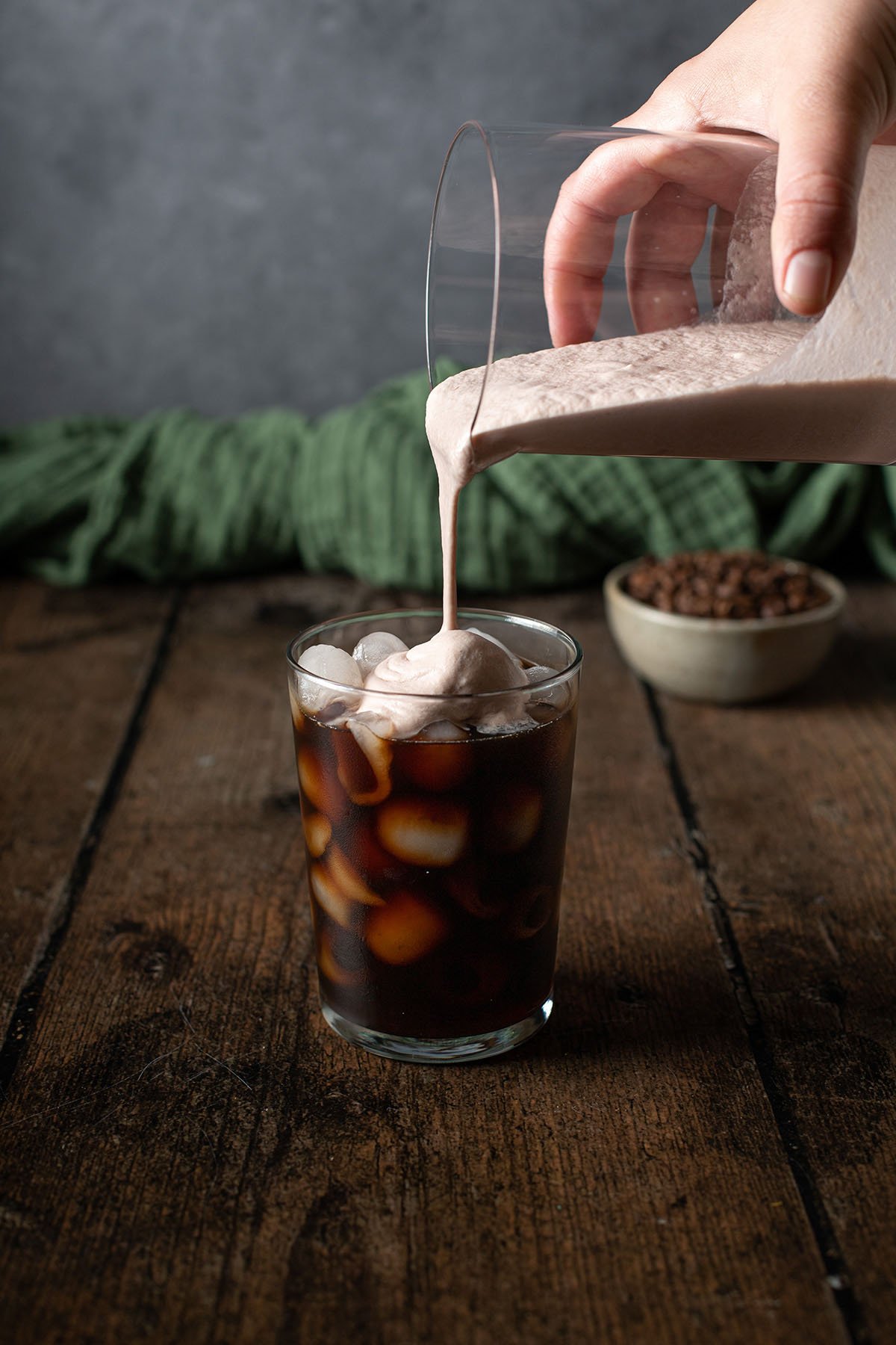 chocolate cream cold foam being poured onto the top of a glass of cold brew coffee