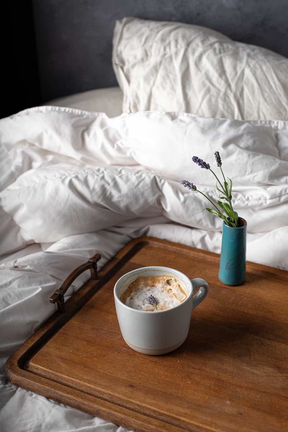 lavender latte on wooden tray sitting on bed with white linens