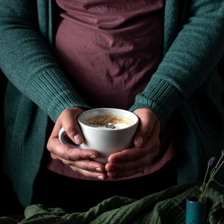 a person holding a lavender latte in a mug with two hands