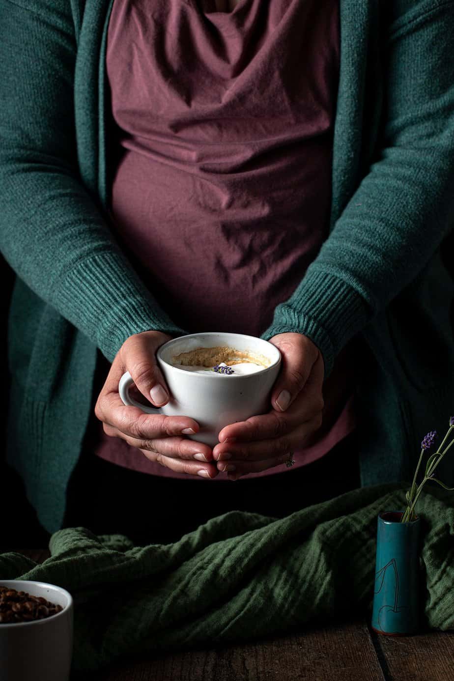 a person holding a lavender latte in a mug with two hands