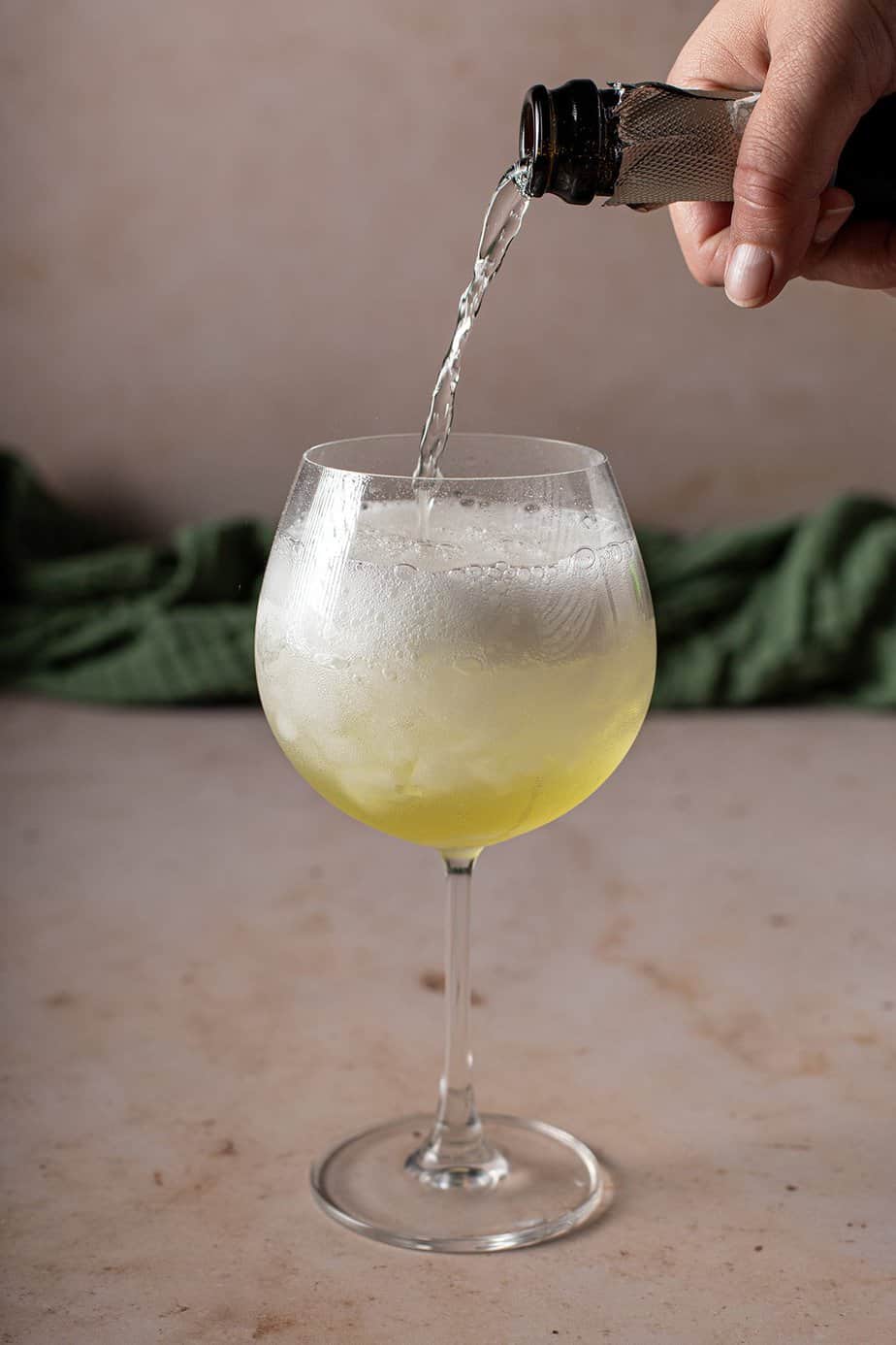 large wine glass filled with crushed ice and some limoncello, prosecco is being poured into it