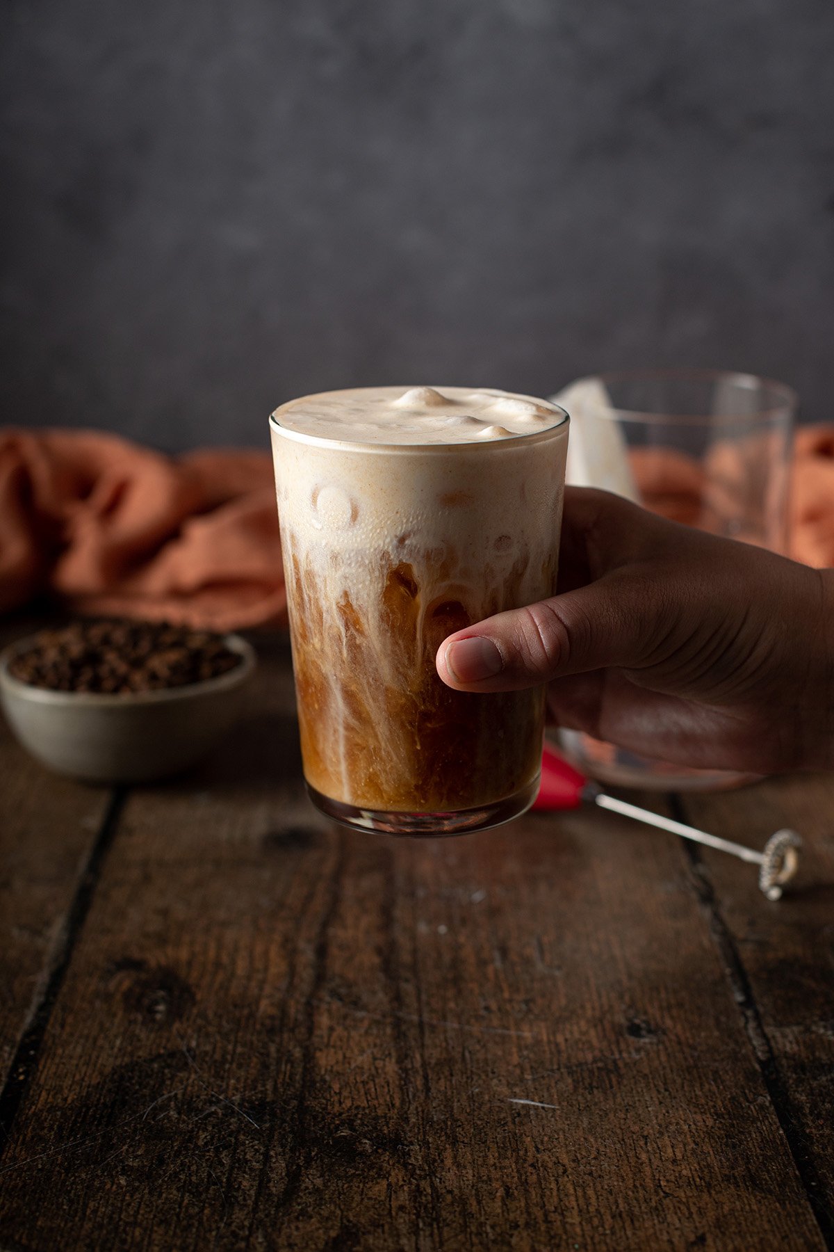 a hand holding a glass of cold brew with pumpkin cream cold foam on top