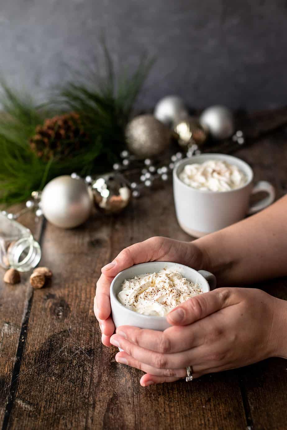 two hands holding a mug of eggnog latte