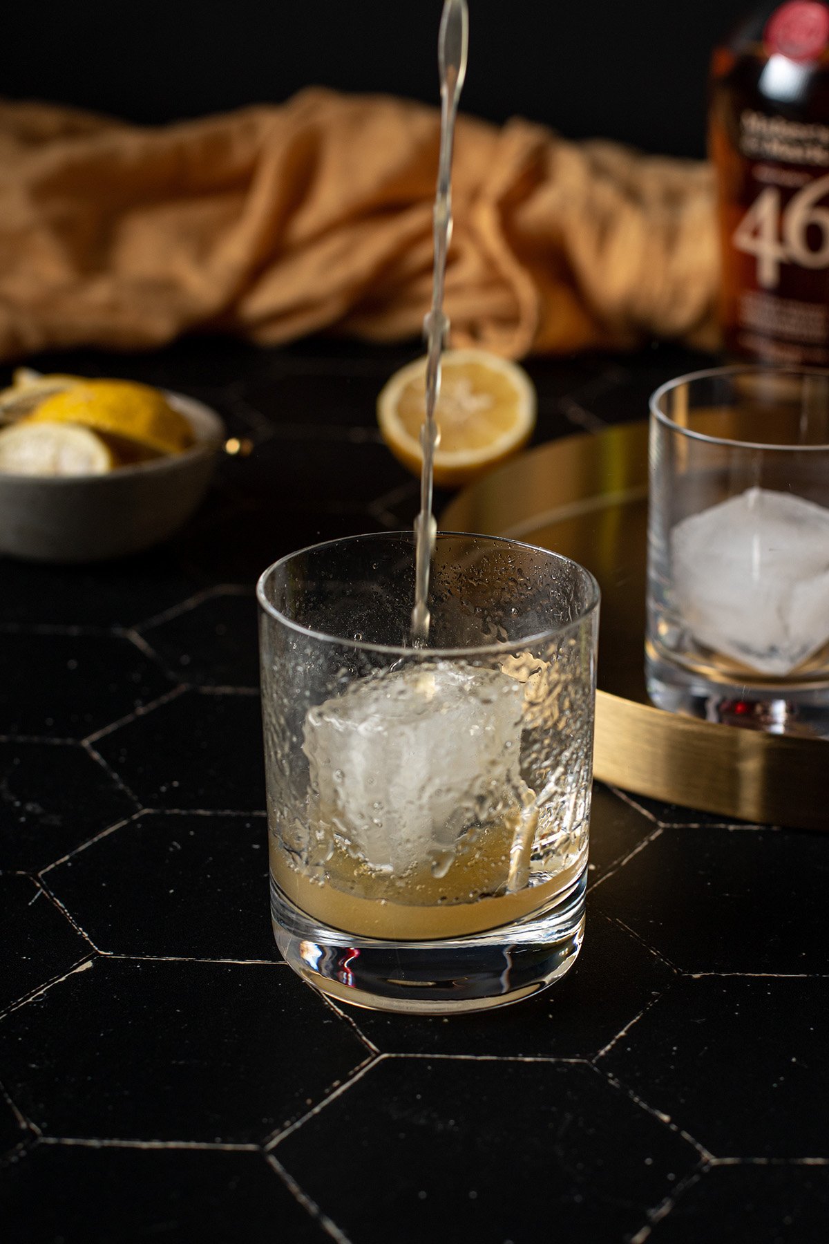 gold rush cocktail being poured over a large ice cube in a rocks glass