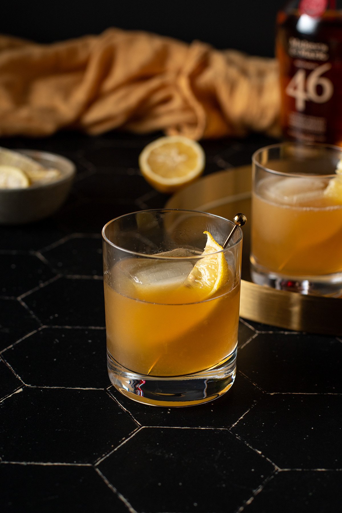 a gold rush cocktail in a rocks glass, garnished with a lemon wedge on a cocktail pick