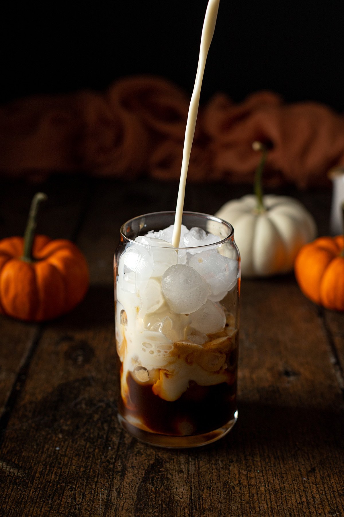 oat milk being poured into a glass with ice, espresso, and pumpkin syrup