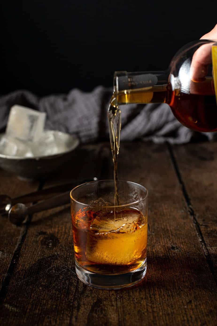 bourbon being poured over a smoked ice cube in a rocks glass