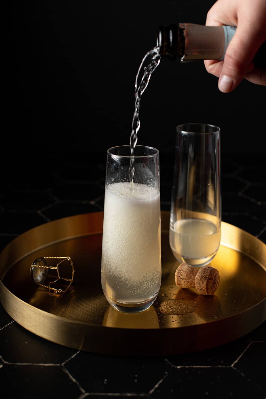 two stemless champagne flutes on a gold serving tray, prosecco being poured into one