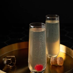 two stemless champagne flutes on a gold serving tray, full of french 76 cocktails, one with a cherry at the bottom of the flute