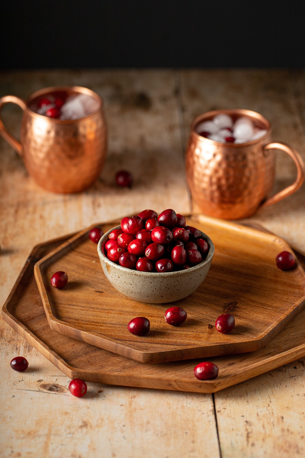 a small bowl of fresh cranberries, two copper mugs in the background