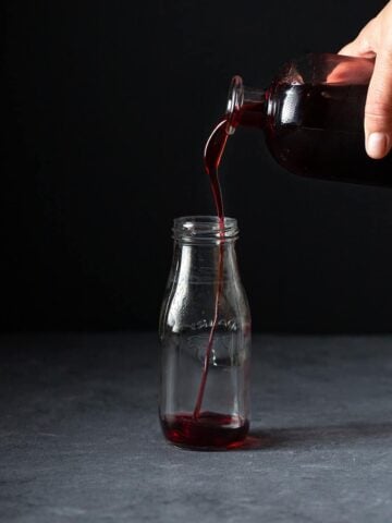 homemade grenadine syrup being poured into a small glass bottle