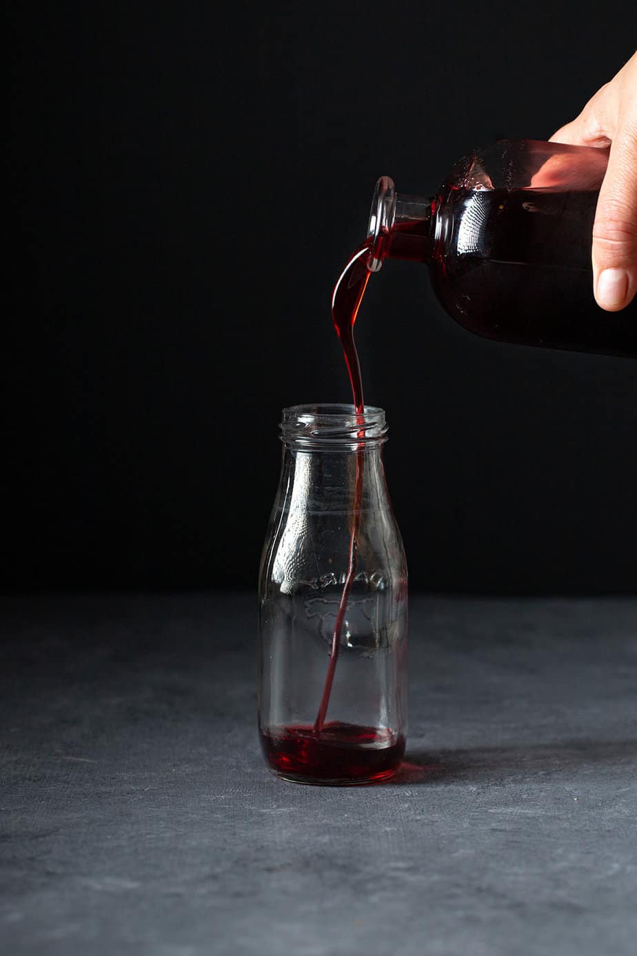 homemade grenadine syrup being poured into a small glass bottle