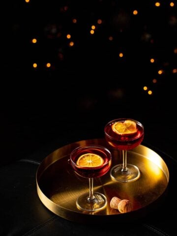 two coupe glasses filled with red liquid garnished with dried orange slices