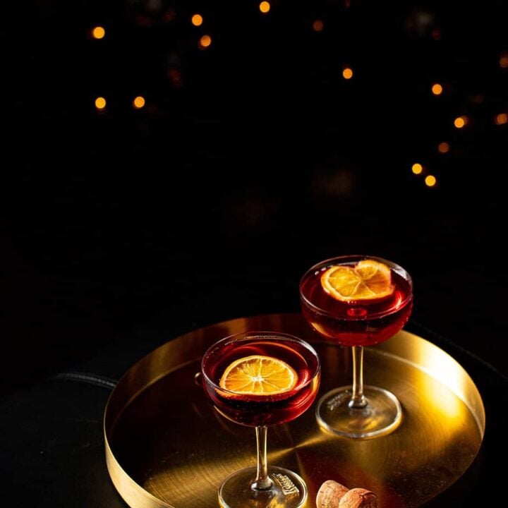 two coupe glasses filled with red liquid garnished with dried orange slices